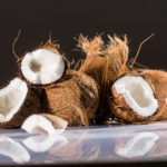 halbierte Kokosnuss neben mehreren liegenden Kokosnüssen