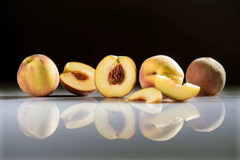 halbierte Pfirsich mit Kern umgeben von ganzen und halben Pfirsichen sowie Pfirsichscheiben